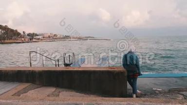 悲伤的年轻女孩看着风雨飘摇的大海。 孤独的女人站在码头。 在荒无人烟的木板路上的女孩。 年轻的悲观女孩